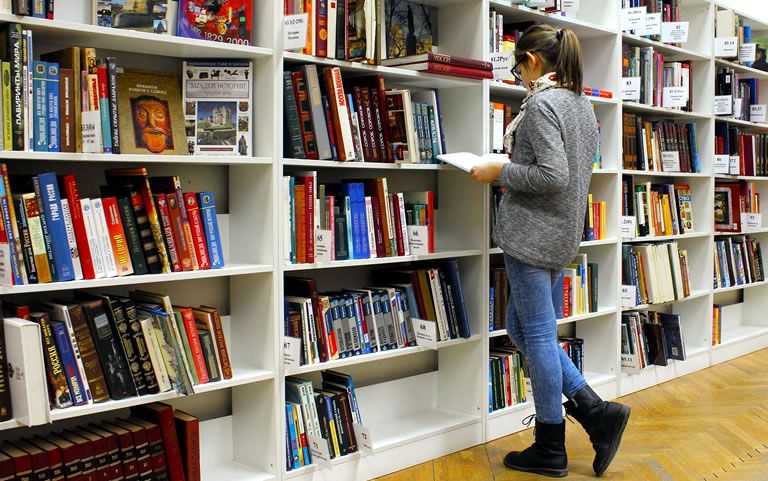 Kind met opengeslagen boek n de hand, staande voor grote boekenkast